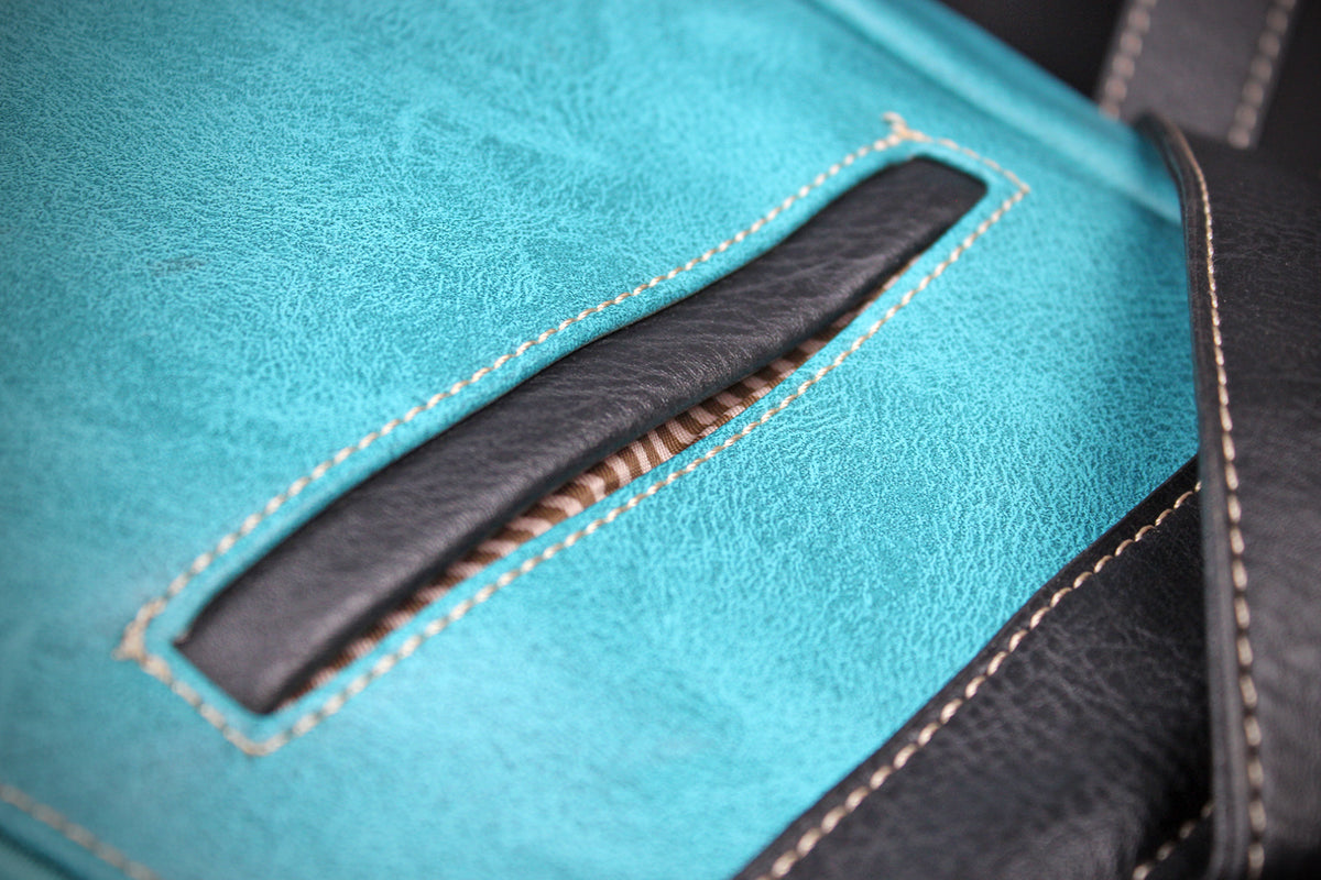 Close-up of a turquoise leather bag with black leather trim and white contrast stitching.