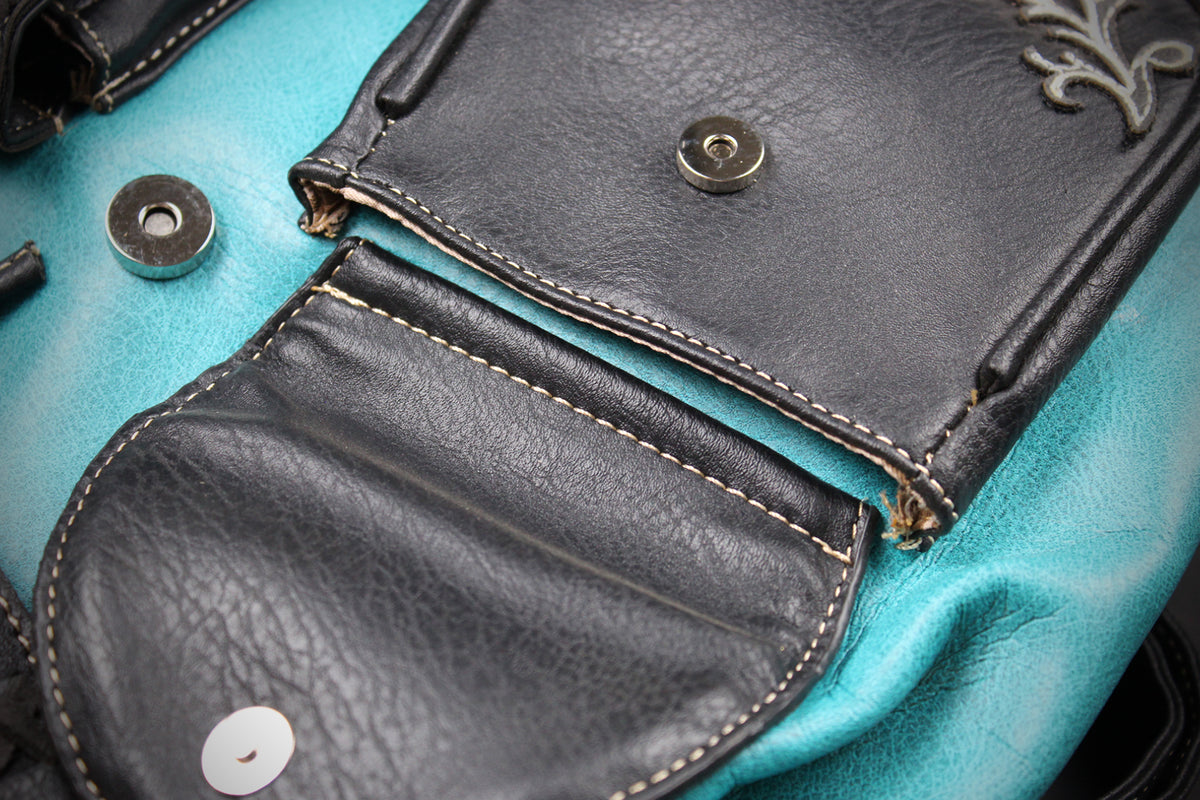 Close-up detail of a handbag showing black leather flap pockets with contrast stitching and snap buttons over a turquoise fabric body.