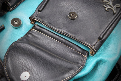 Close-up detail of a handbag showing black leather flap pockets with contrast stitching and snap buttons over a turquoise fabric body.