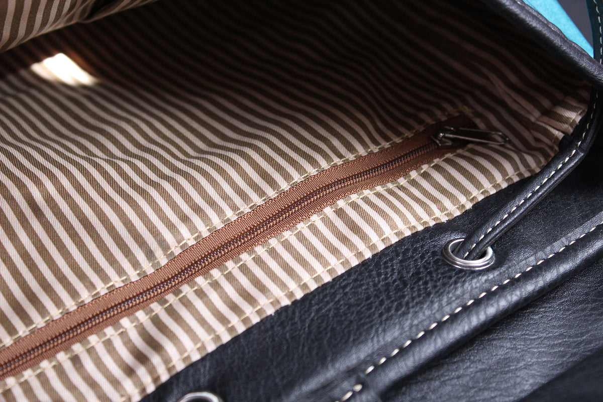 Close-up of a handbag interior showing a brown zipper along a beige and brown striped fabric lining, with a black leather exterior edge and silver metal hardware.