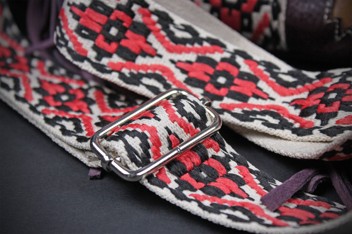 Close-up of a woven strap with a geometric pattern in red, black, and off-white, featuring a silver metal buckle.