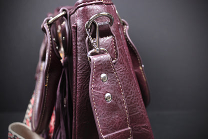 Close-up of a burgundy pebbled leather handbag showing the side profile, silver-tone hardware, and a patterned fabric lining or strap detail against a dark background.