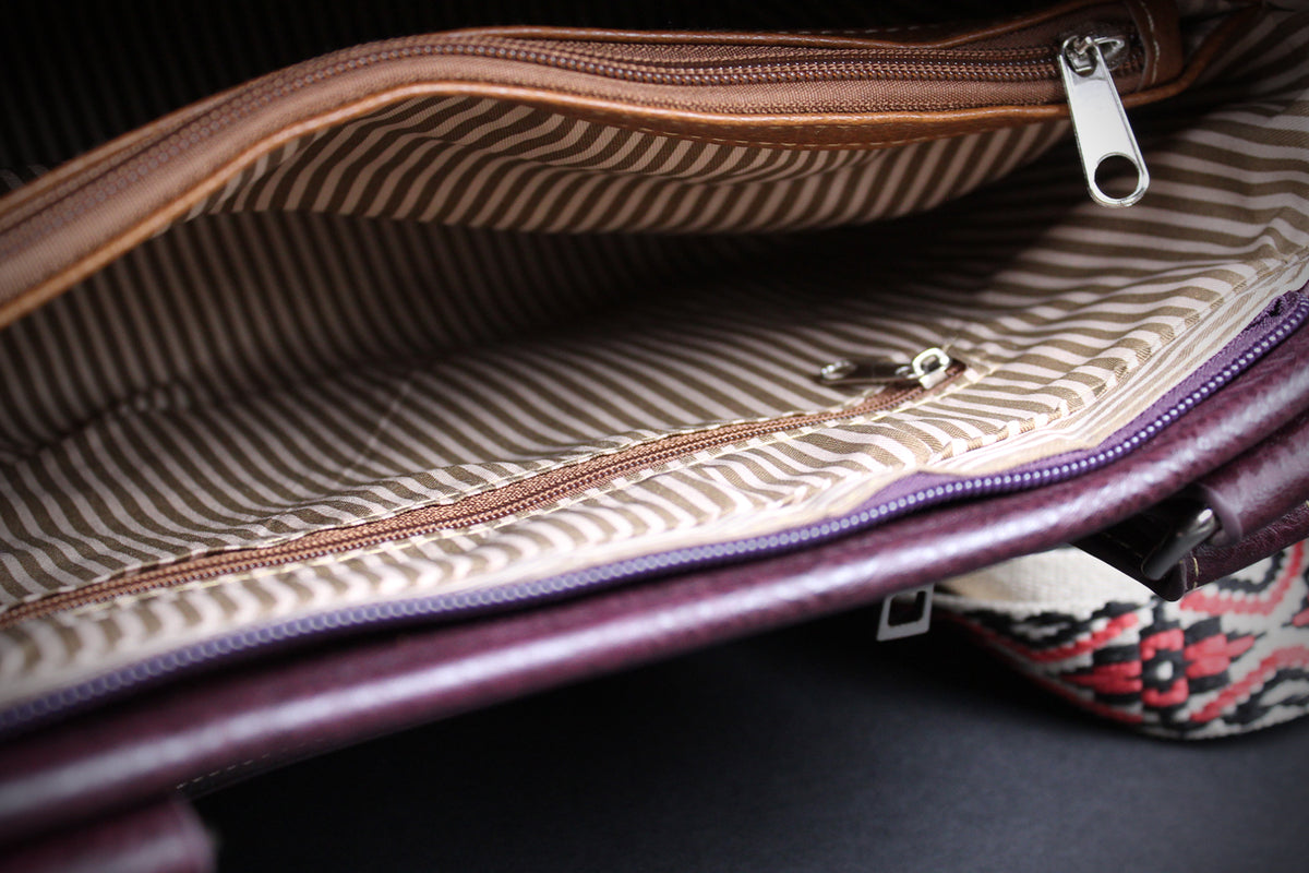 Close-up of an open purple leather bag showing a brown and beige striped interior lining with metal zippers.