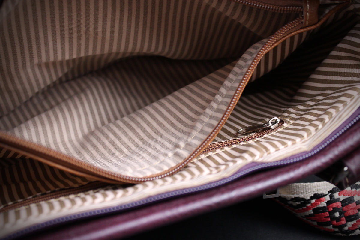 Close-up of the interior lining of a striped fabric bag, showing a brown zipper, beige and brown pinstriped material, and a dark purple outer edge.