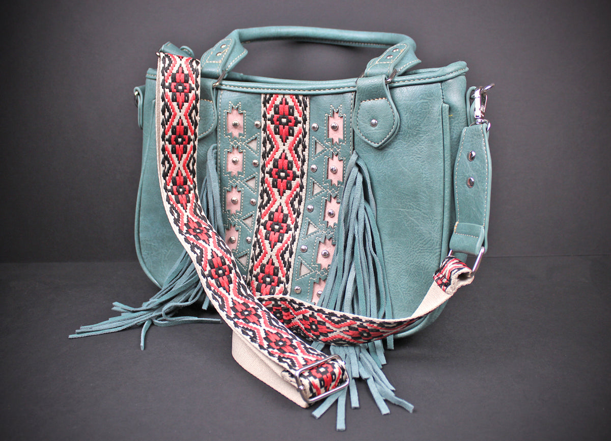 A teal faux-leather handbag with a wide, patterned woven shoulder strap, featuring fringe details and geometric embroidery on the front, set against a dark gray background.