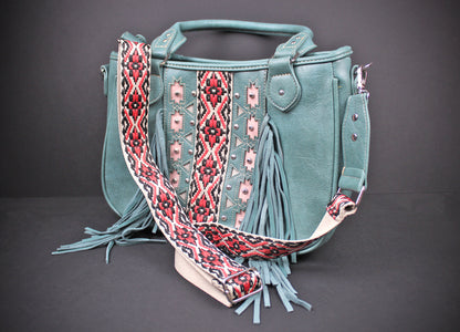 A teal faux-leather handbag with a wide, patterned woven shoulder strap, featuring fringe details and geometric embroidery on the front, set against a dark gray background.