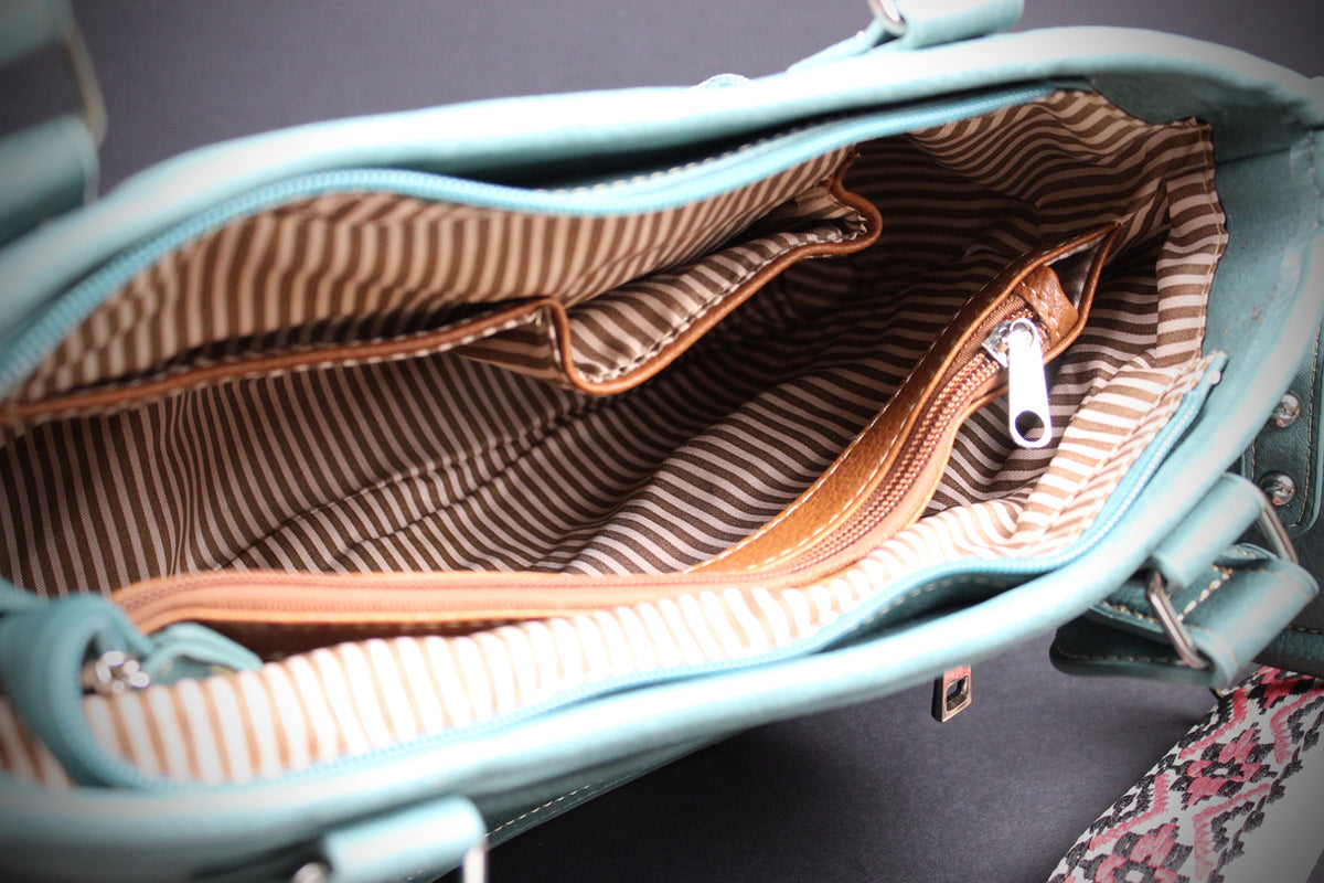 Close-up of the interior of a light blue handbag, showing a striped fabric lining in beige and brown with a brown zipper and silver metal pull.