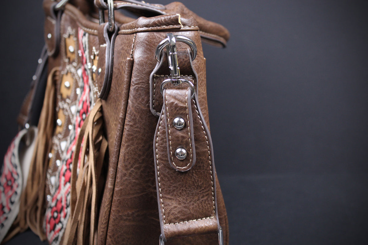 Close-up of a brown leather shoulder bag featuring fringe, silver-tone hardware, and a patterned textile detail against a dark background.