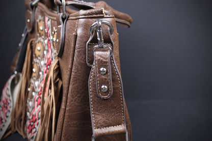 Close-up of a brown leather shoulder bag featuring fringe, silver-tone hardware, and a patterned textile detail against a dark background.