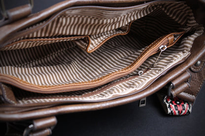 Close-up of the interior of a brown leather bag, showing a striped fabric lining in beige and brown with a zippered pocket and interior compartments.