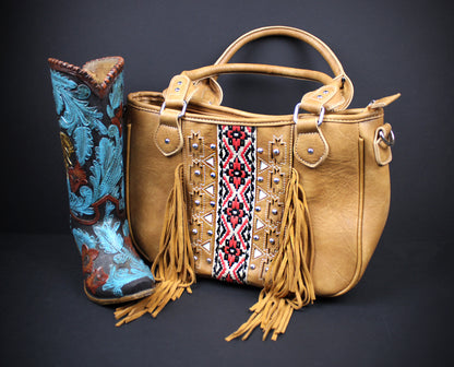 A tan leather handbag with fringe and a central geometric embroidered panel, displayed next to a tall western boot with turquoise, brown, and gold embossed detailing on a dark background.