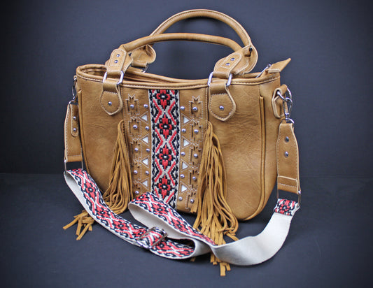 A tan leather handbag with dual top handles, a wide embroidered shoulder strap, and long tan fringe, photographed against a dark gray studio background.