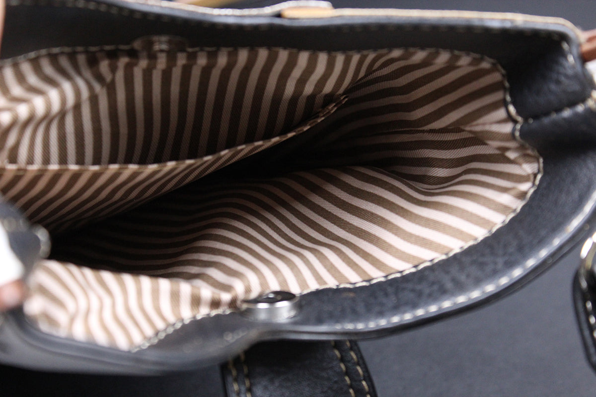 Close-up of the interior of a black leather bag showing a brown and beige striped fabric lining.