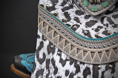 Close-up of a western-style boot featuring a black and white leopard print, a gray decorative band with silver studs, turquoise stitching, and a turquoise insole edge.