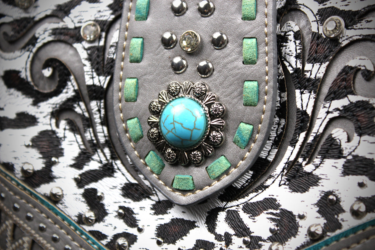 Close-up detail of a western-style bag or belt featuring a gray leather flap with turquoise studs, a central turquoise cabochon surrounded by silver-toned metal, and a black-and-white patterned body.