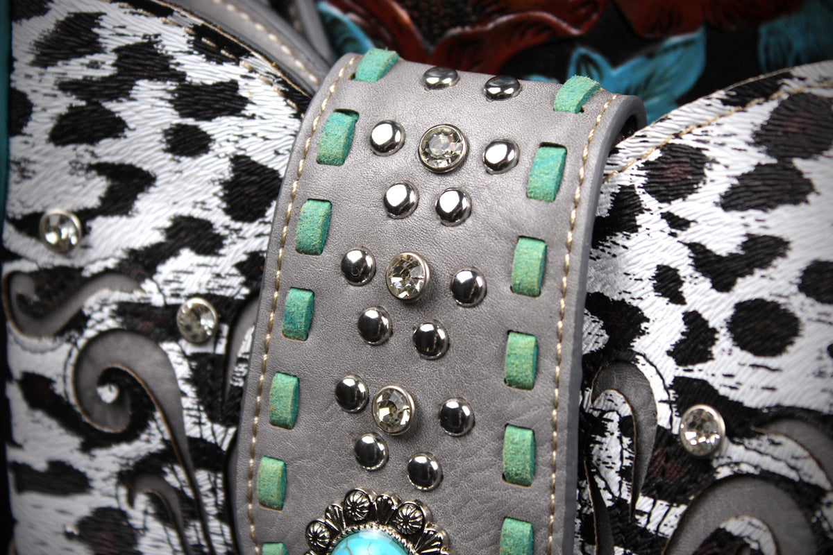 A close-up of a western-style leather belt featuring a wide gray center strap studded with silver-toned rhinestones and turquoise-colored rectangular accents, flanked by black-and-white cowhide patterned sections.