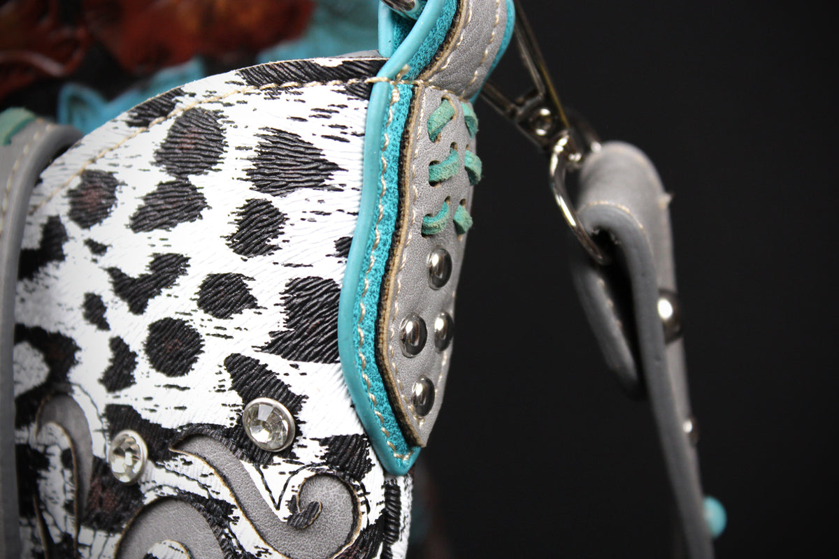 Close-up of a western-style bag featuring a black and white leopard print pattern, gray leather trim, turquoise stitching, and silver-tone studs and hardware against a dark background.
