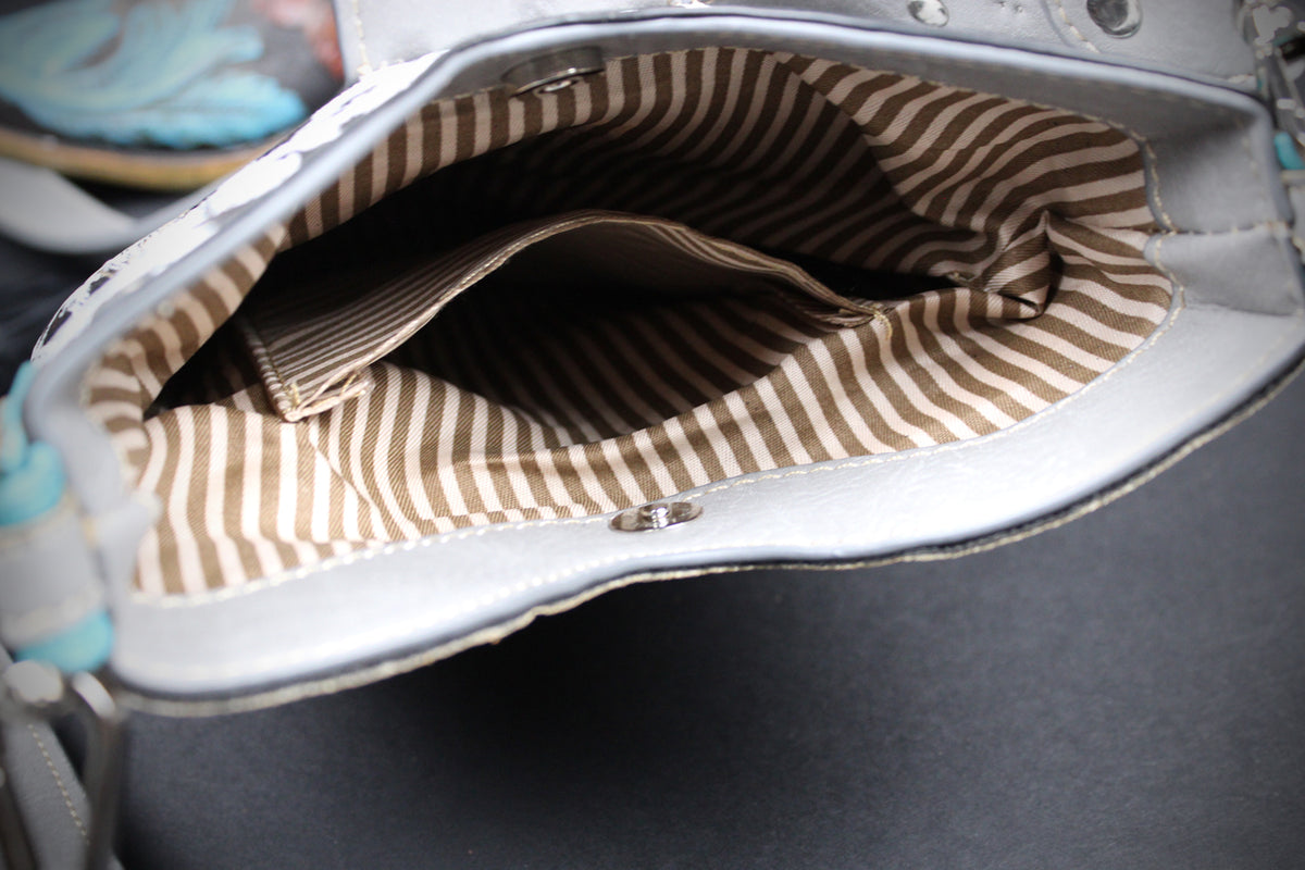 Close-up of the interior lining of a silver handbag, showing a brown and beige striped fabric pocket inside.