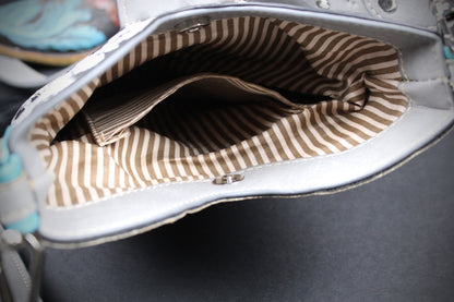 Close-up of the interior lining of a silver handbag, showing a brown and beige striped fabric pocket inside.