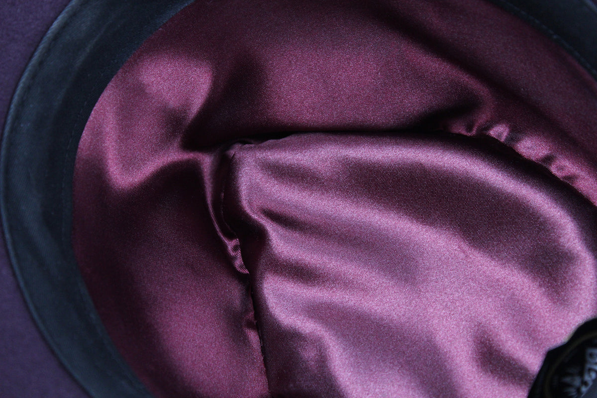Close-up of a satin or silk-like fabric lining in a deep plum purple color, draped inside a dark hat or container.