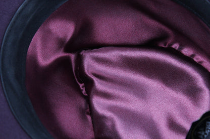 Close-up of a satin or silk-like fabric lining in a deep plum purple color, draped inside a dark hat or container.