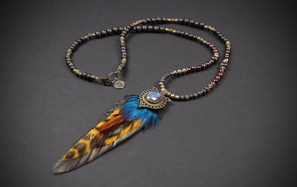 A bohemian-style beaded necklace with a large feather pendant. The necklace features dark metallic beads and a central oval stone surrounded by an ornate filigree frame.