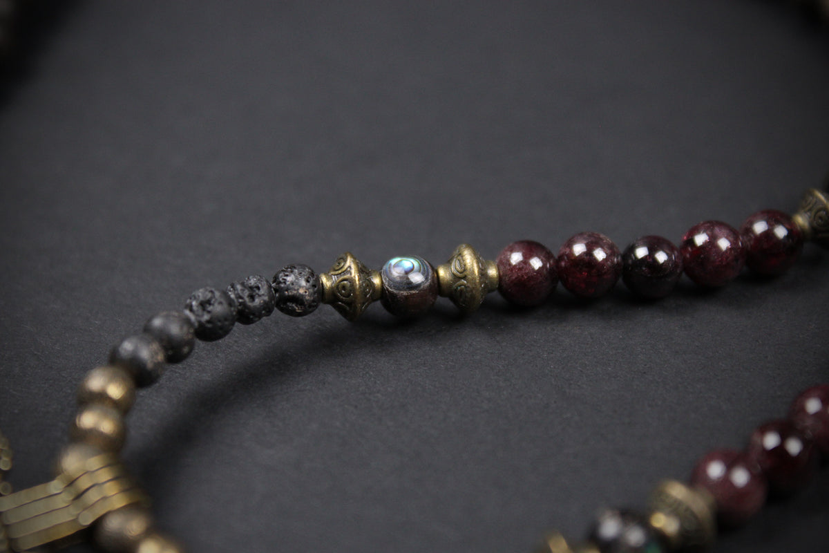 Close-up of a beaded strand with dark gray and deep burgundy beads separated by ornate antique gold metal spacers, set against a dark gray background.