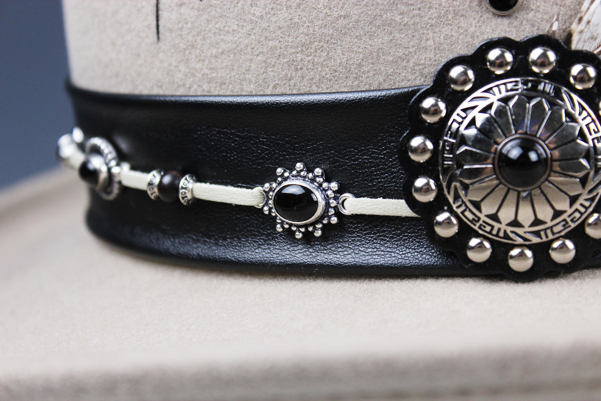 A close-up of a black leather belt with silver-toned metal hardware, including a large decorative medallion and smaller matching accents, displayed on a beige mannequin stand.