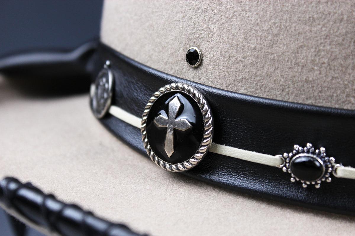 Close-up of a beige felt hat with a black leather band featuring silver-toned conchos and black oval stones.